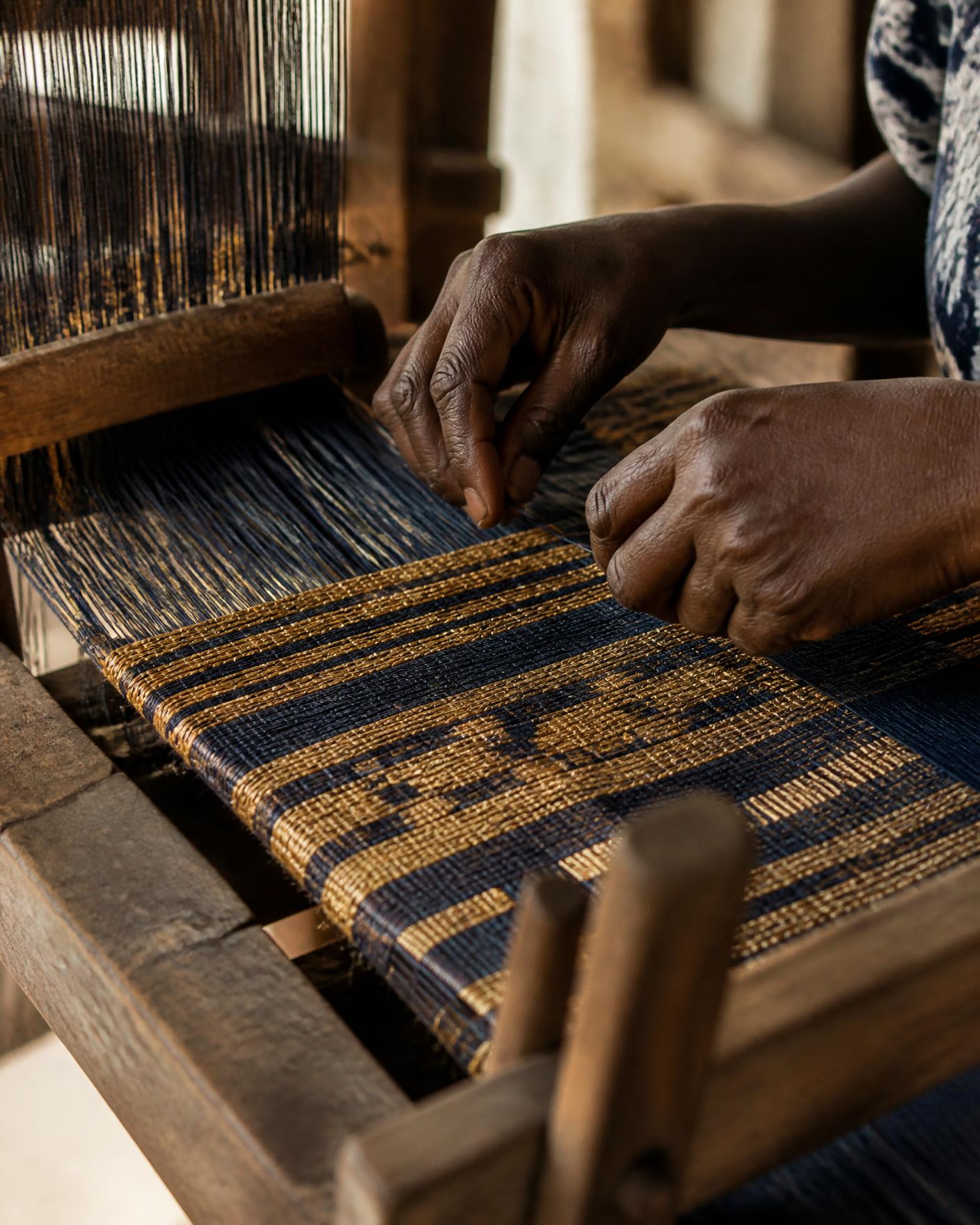 Hands weaving narrow-strip kente on a wooden loom