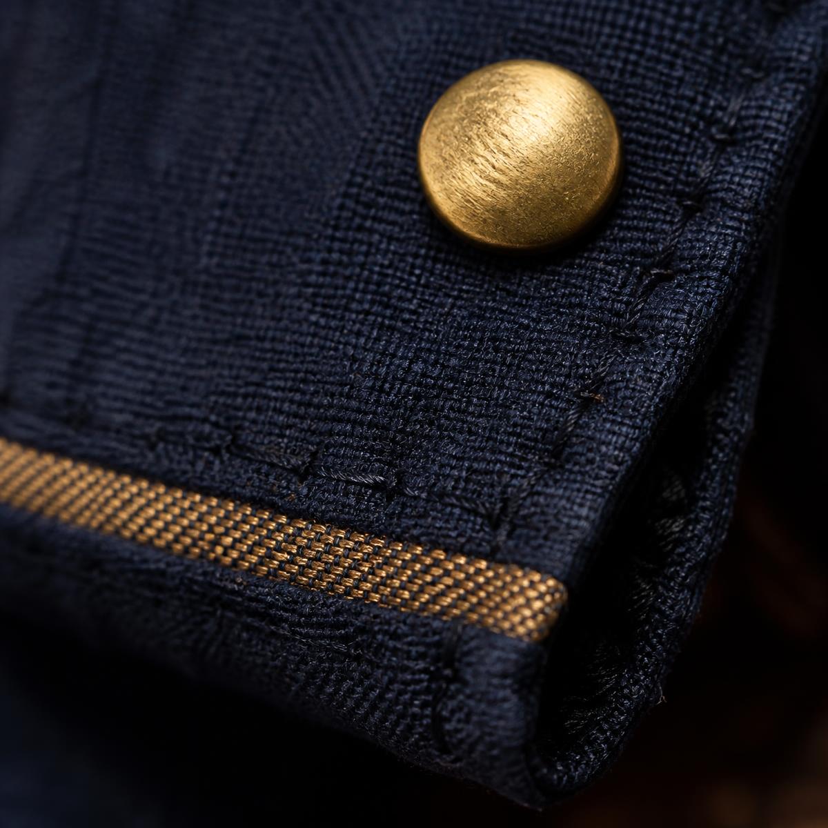 Close detail of a hand-stitched navy hem with a cast brass button